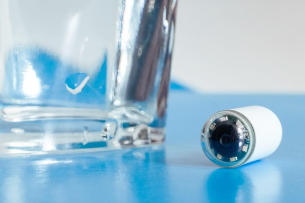 Capsule with camera for capsular endoscopy and glass of water on blue surface